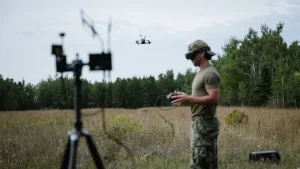 Een marinier bestuurt een drone met een controller en FPV-bril, met op de voorgrond een mobiel defensie-zendmastje.