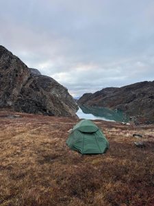 Een groene militaire tent boven op een berg met uitzicht over een groot fjord in het steile en koude landschap van Groenland.