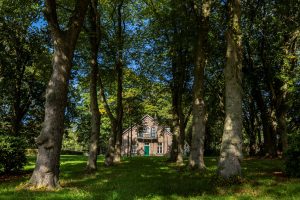 Een klassieke kazernewoning met een lange laan van groene bomen ervoor op het terrein van Kamp Nieuw-Milligen.